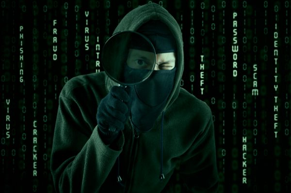 Internet Theft - a hooded man looking at computer screen using magnifying glass